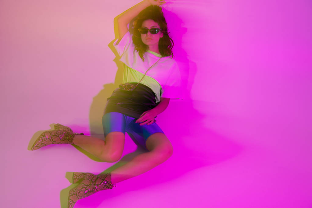 movimento sfocatura di elegante giovane donna in occhiali da sole sdraiato su viola
 - Foto, immagini