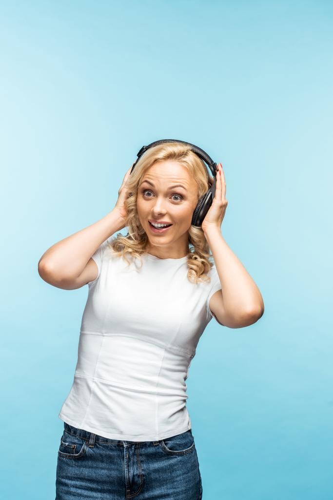 femme blonde surprise écoutant de la musique dans des écouteurs noirs sur bleu
  - Photo, image
