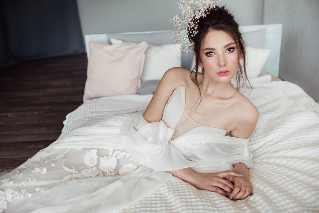 элегантная брюнетка невеста лежит на белой кровати в спальне
  - Фото, изображение