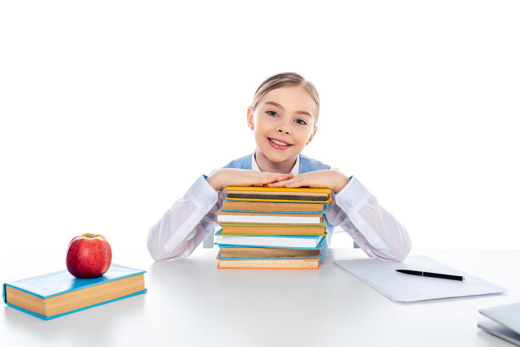 улыбающаяся школьница, сидящая за столом с книгами и смотрящая на камеру, изолированную от белого
 - Фото, изображение