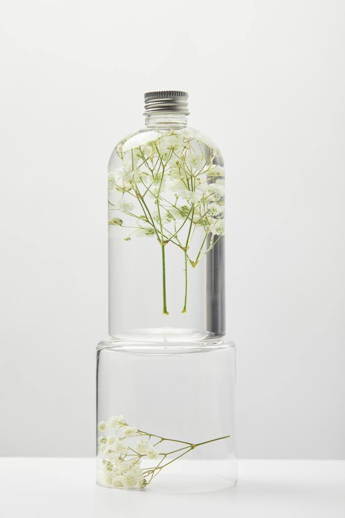 prodotto cosmetico biologico in bottiglia trasparente con fiori di campo sul cavalletto isolato su grigio
 - Foto, immagini
