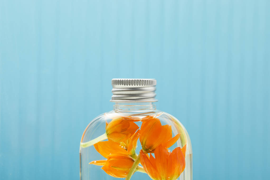 κοντά στο βιολογικό προϊόν ομορφιάς με πορτοκαλί λουλούδια σε φιάλη σε μπλε φόντο με χώρο αντιγραφής - Φωτογραφία, εικόνα