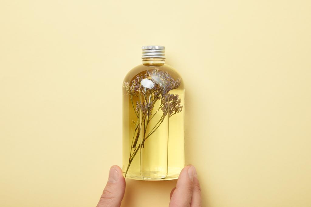 vágott kilátás az ember gazdaság palack természetes szépségápolási termék és gyógynövények sárga háttér - Fotó, kép