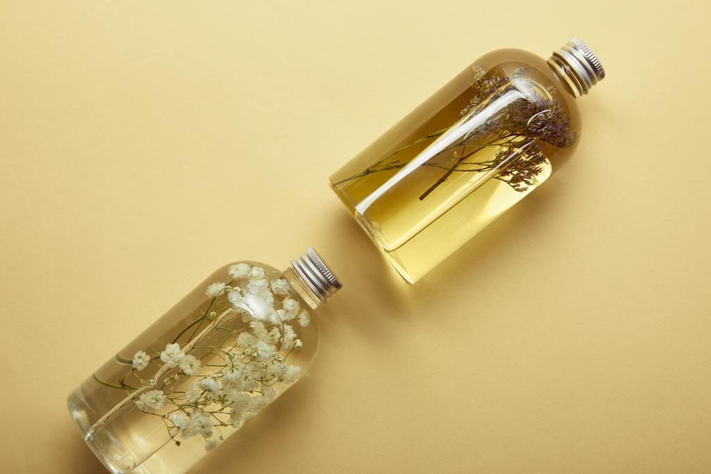 вид зверху на прозорі пляшки з органічними продуктами краси та сушеними лісовими квітами на жовтому фоні
  - Фото, зображення