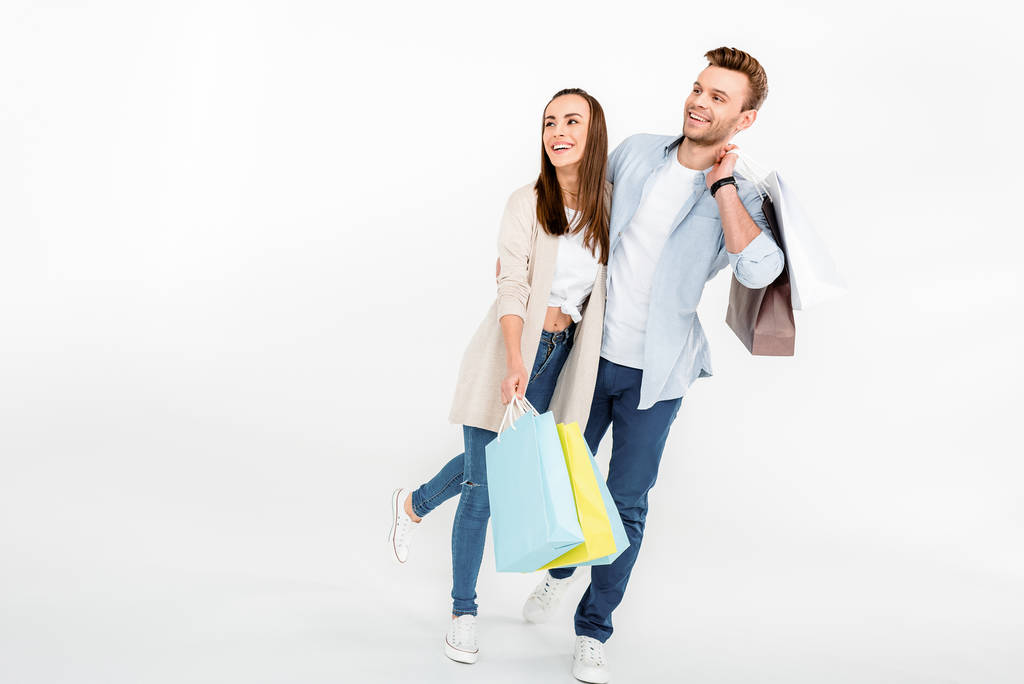 glückliches junges Paar mit Einkaufstüten, die sich umarmen und wegschauen - Foto, Bild