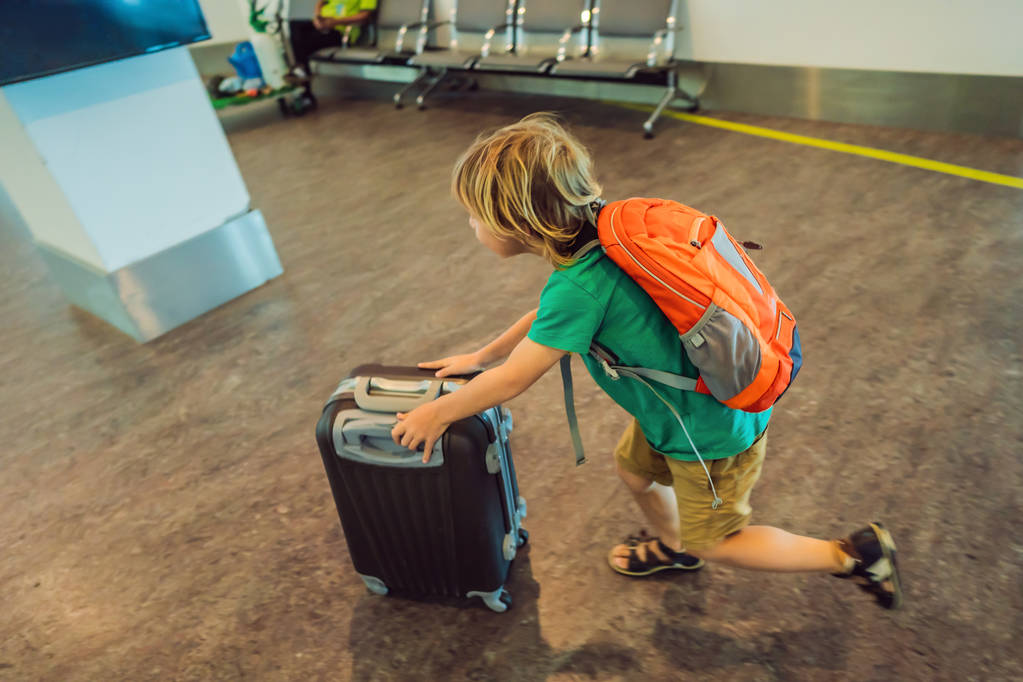 lustiger kleiner Junge auf Urlaubsreise mit Koffer am Flughafen, drinnen - Foto, Bild