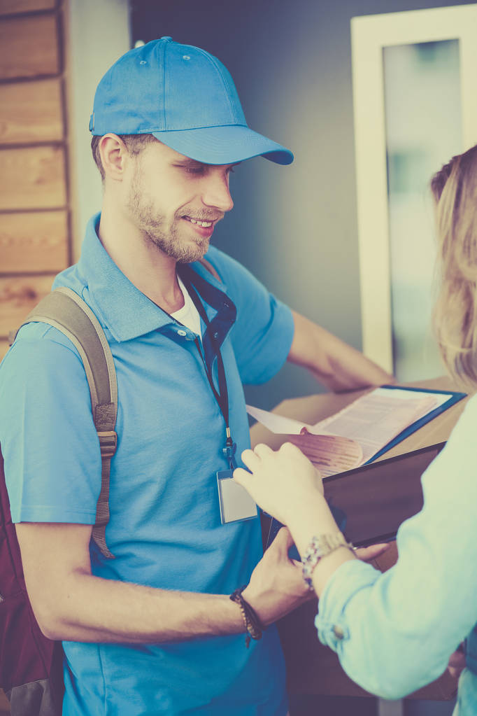 Repartidor sonriente en uniforme azul que entrega la caja de paquetes al destinatario - concepto de servicio de mensajería - Foto, Imagen