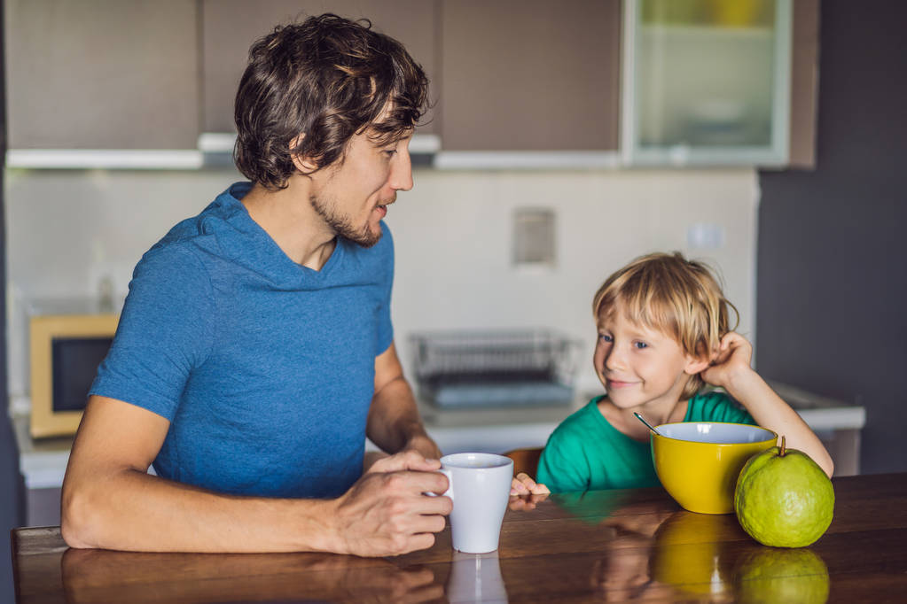 Padre e hijo están hablando y sonriendo mientras desayunan en la cocina
 - Foto, Imagen