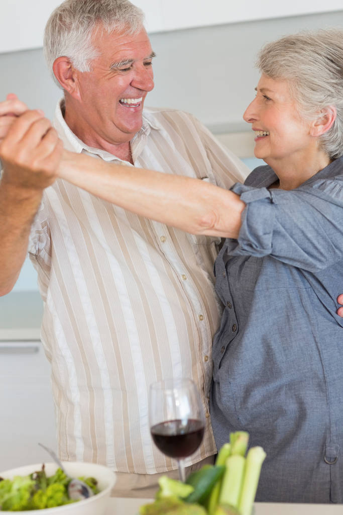Szczęśliwy starszy para taniec przygotowując posiłek w domu w kuchni - Zdjęcie, obraz