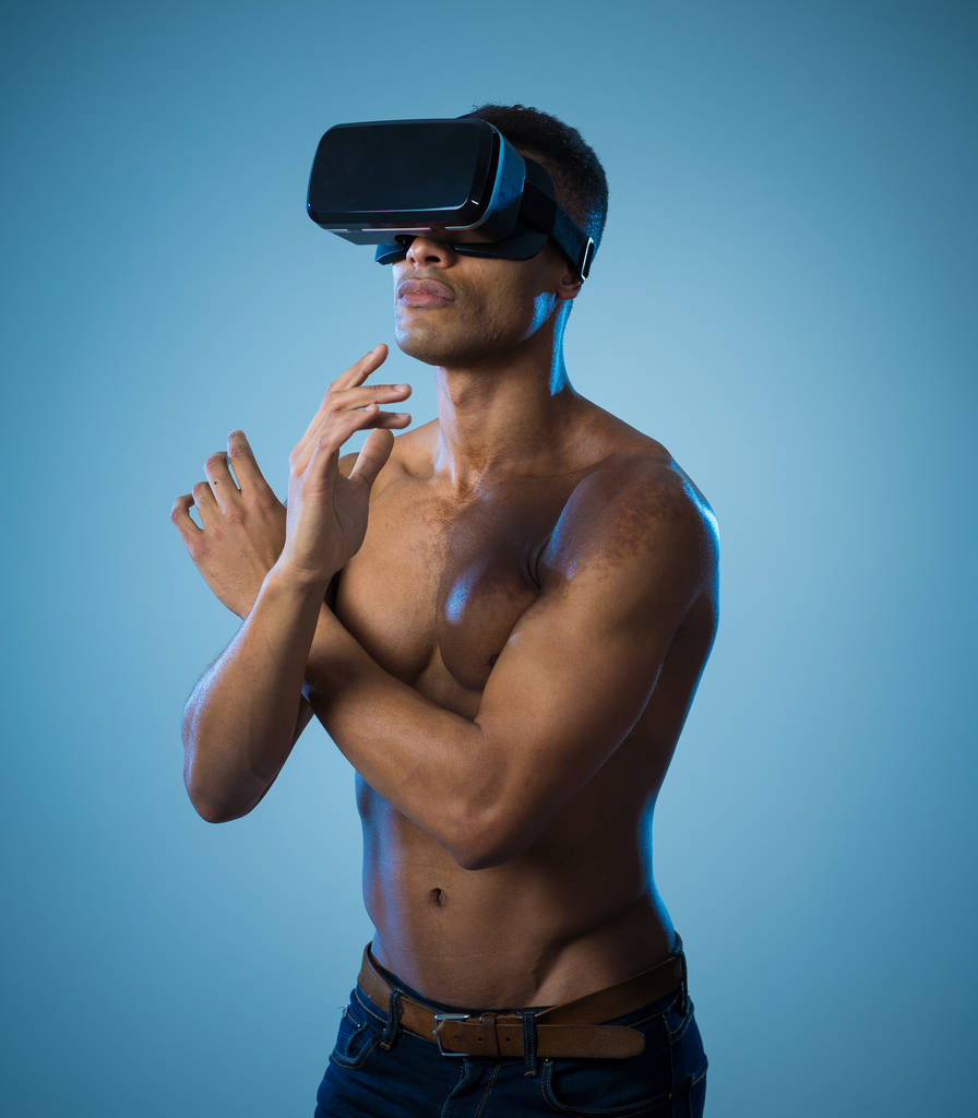 Attraente uomo afro-americano che utilizza occhiali VR aumentati esplorando il mondo 3d sentendosi entusiasta della simulazione, nuove sensazioni e desideri. In realtà virtuale, innovazione e nuovo concetto di tecnologia
. - Foto, immagini