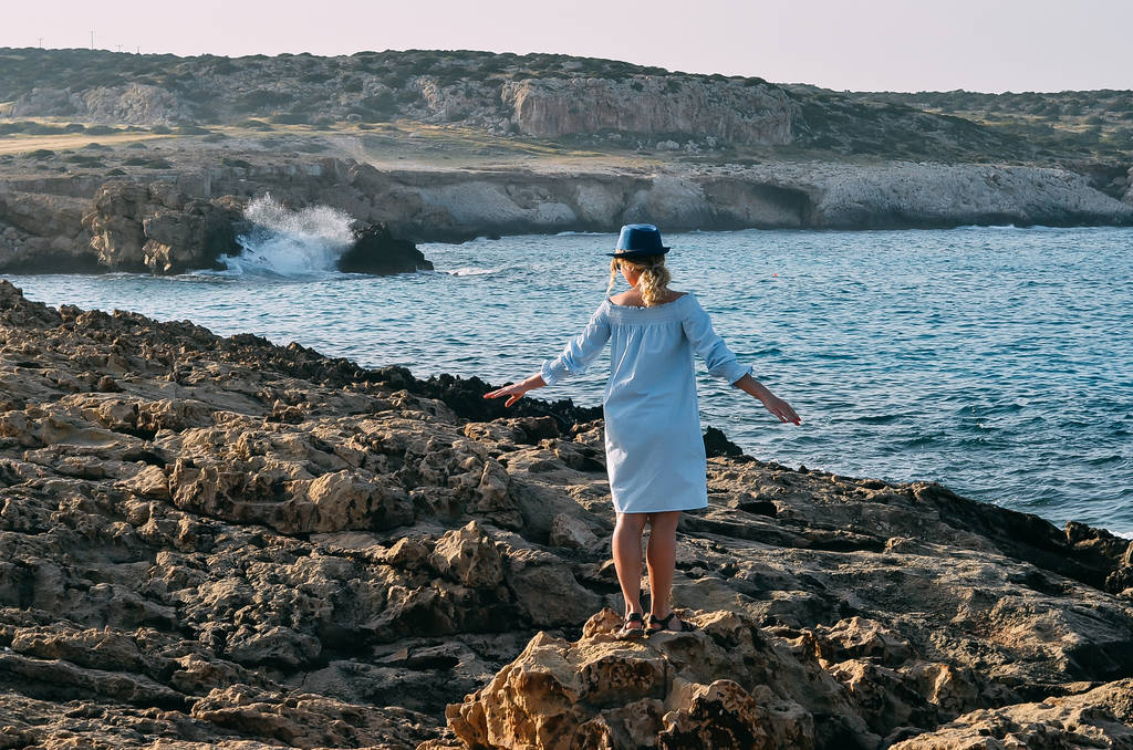 Vista posteriore di giovane donna viaggiatore vicino al mare in piedi su una scogliera a
 - Foto, immagini