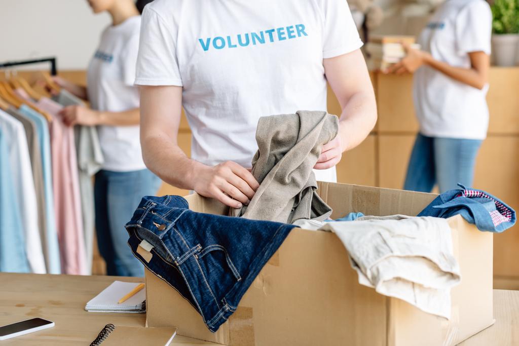 bijgesneden weergave van vrijwillige uitpakken kartonnen doos met kleding - Foto, afbeelding