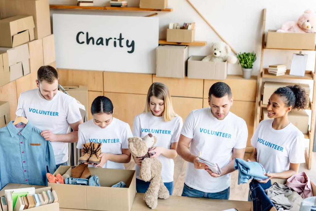 grupo de jóvenes voluntarios multiculturales desempacando cajas de cartón con ropa, libros y juguetes
 - Foto, imagen