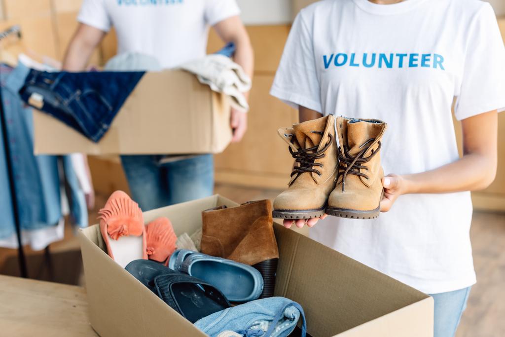 wykadrowany widok wielokulturowych wolontariuszy rozpakowywanie kartonów z ubraniami i obuwiem - Zdjęcie, obraz