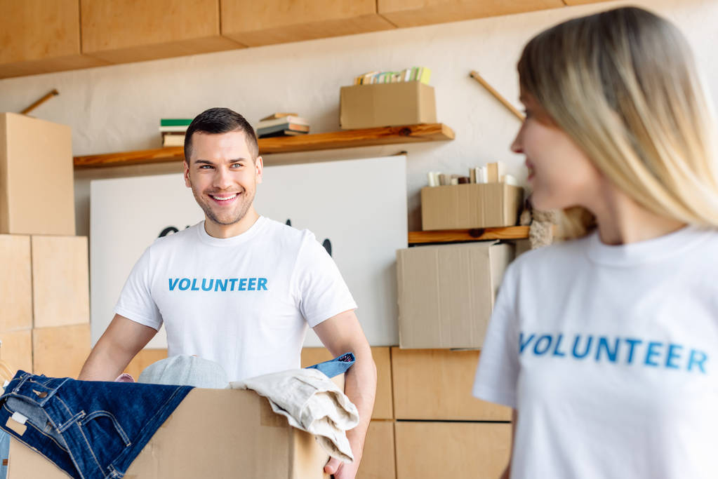 вибірковий фокус молодого красивого чоловіка, який тримає картонну коробку біля гарного добровольця
 - Фото, зображення