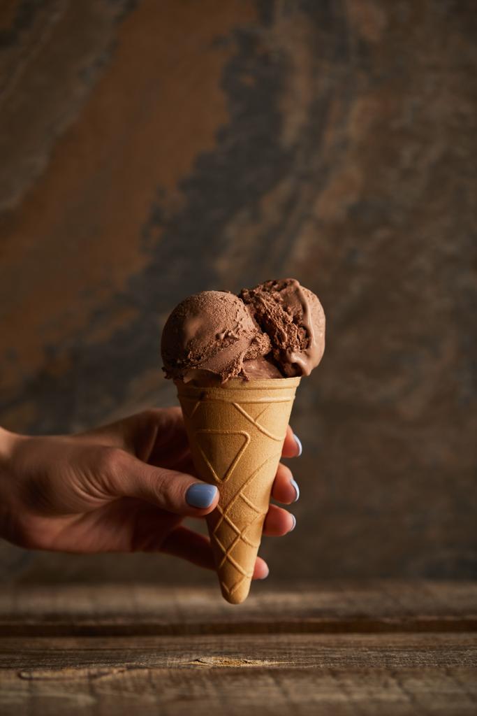 oříznutý pohled na ženu držící čokoládovou zmrzlinu z dřevěného stolu - Fotografie, Obrázek