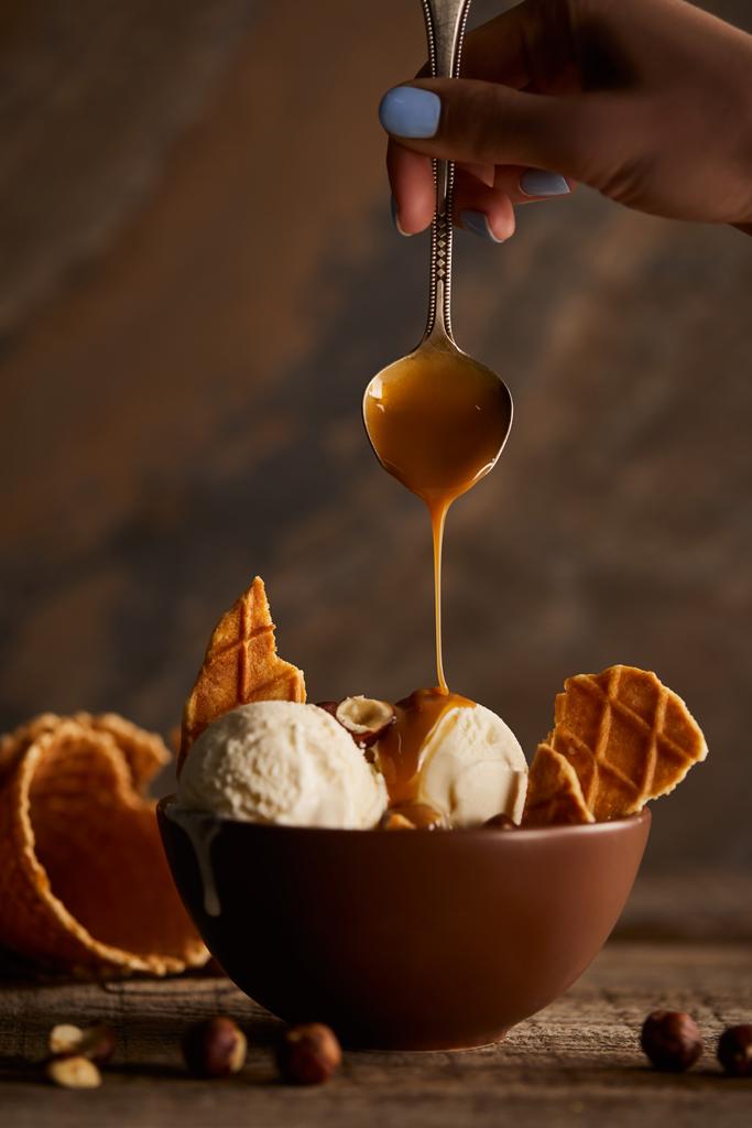 Vue recadrée de la femme versant du caramel sur une délicieuse crème glacée avec des morceaux de gaufre
 - Photo, image
