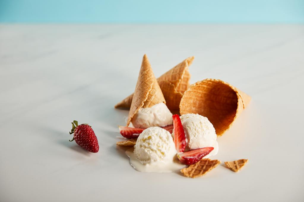 ワッフルコーンとおいしい溶けるアイスクリームと灰色のテーブルの上にイチゴ - 写真・画像