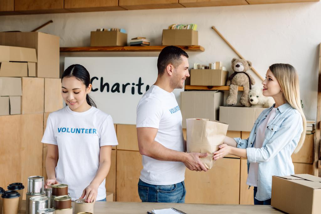 mladí multikulturní dobrovolníci dávat jídlo hezké ženě v charitativním centru - Fotografie, Obrázek