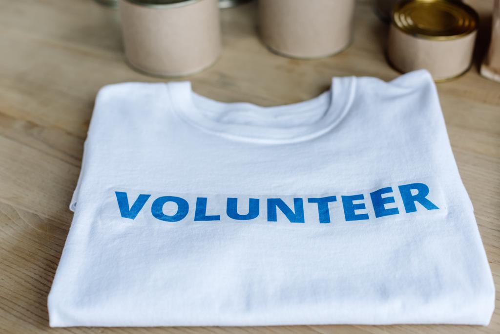 enfoque selectivo de camiseta blanca con inscripción de voluntario azul en la mesa de madera
 - Foto, imagen