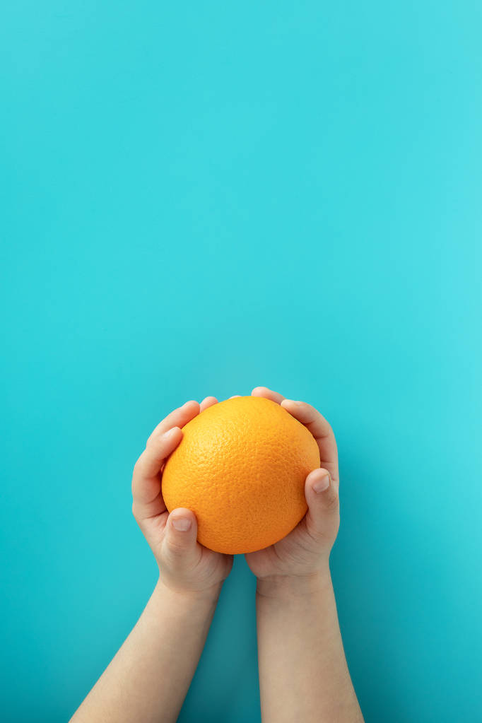 Bir çocuğun elinde mavi arka plan turuncu. Sağlıklı beslenme konsepti - Fotoğraf, Görsel