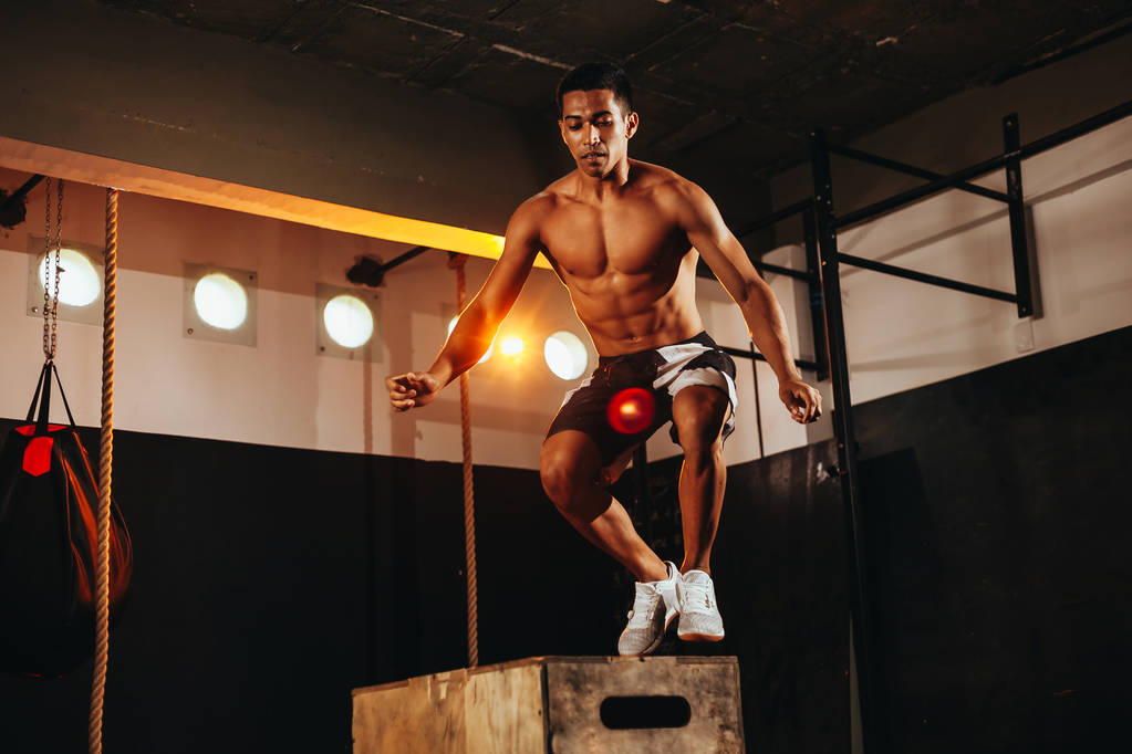 Fitter junger Mann bei einer Boxsprungübung. Sportler macht Kniebeuge im Fitnessstudio - Foto, Bild