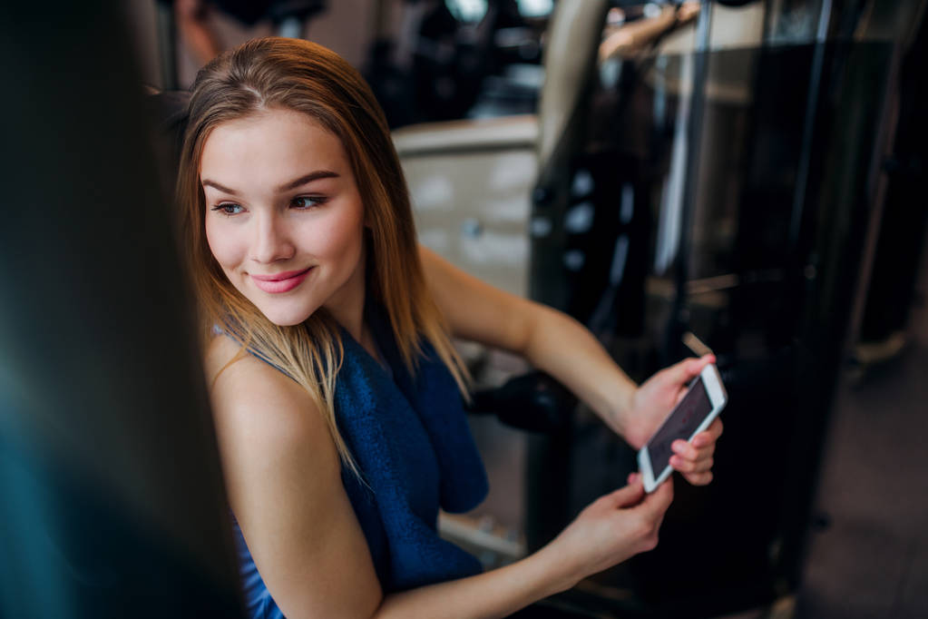 Ένα πορτρέτο του νεαρού κοριτσιού ή της γυναίκας με smartphone σε ένα γυμναστήριο. - Φωτογραφία, εικόνα