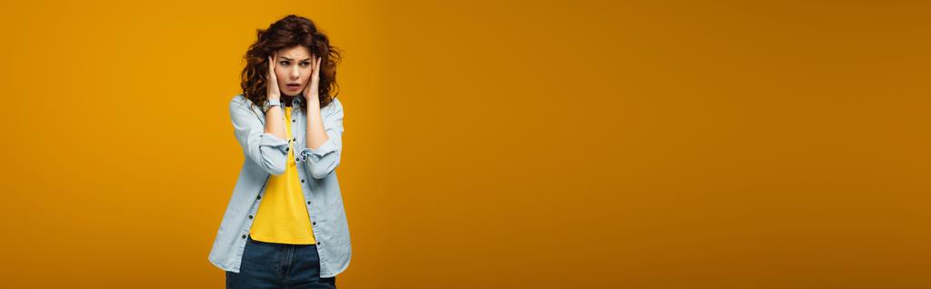 tiro panorâmico de mulher encaracolado chateado tocando cabeça enquanto tendo enxaqueca em laranja
  - Foto, Imagem