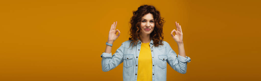 πανοραμική βολή από χαρούμενο σγουρά κοκκινομάλλα γυναίκα στέκεται και δείχνει OK πινακίδες για πορτοκαλί  - Φωτογραφία, εικόνα