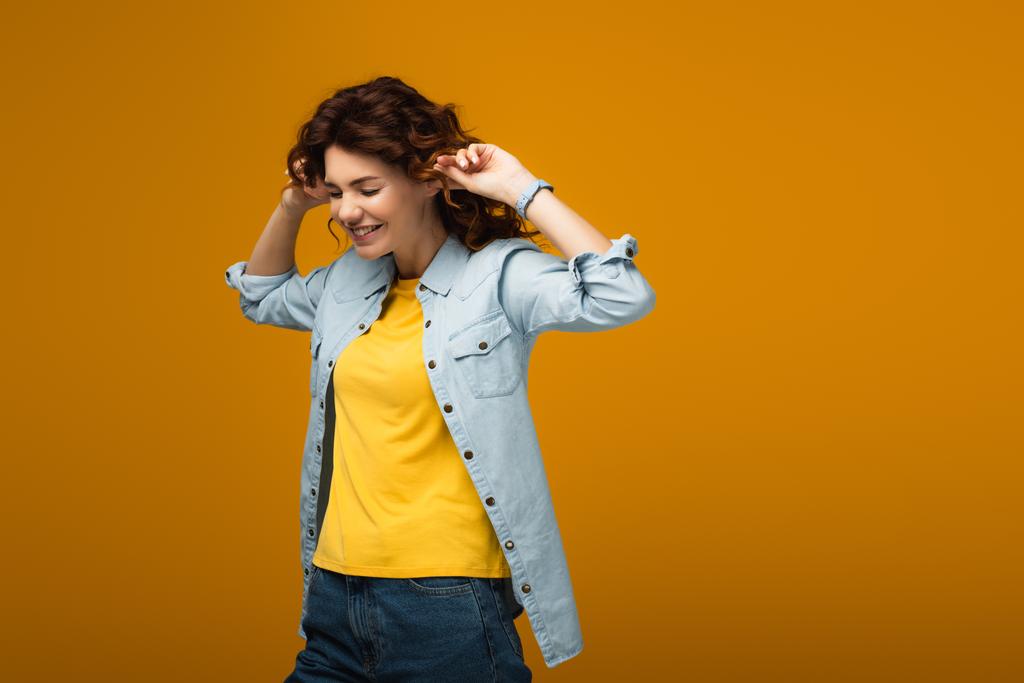 alegre pelirroja mujer tapando orejas mientras de pie en naranja
  - Foto, imagen