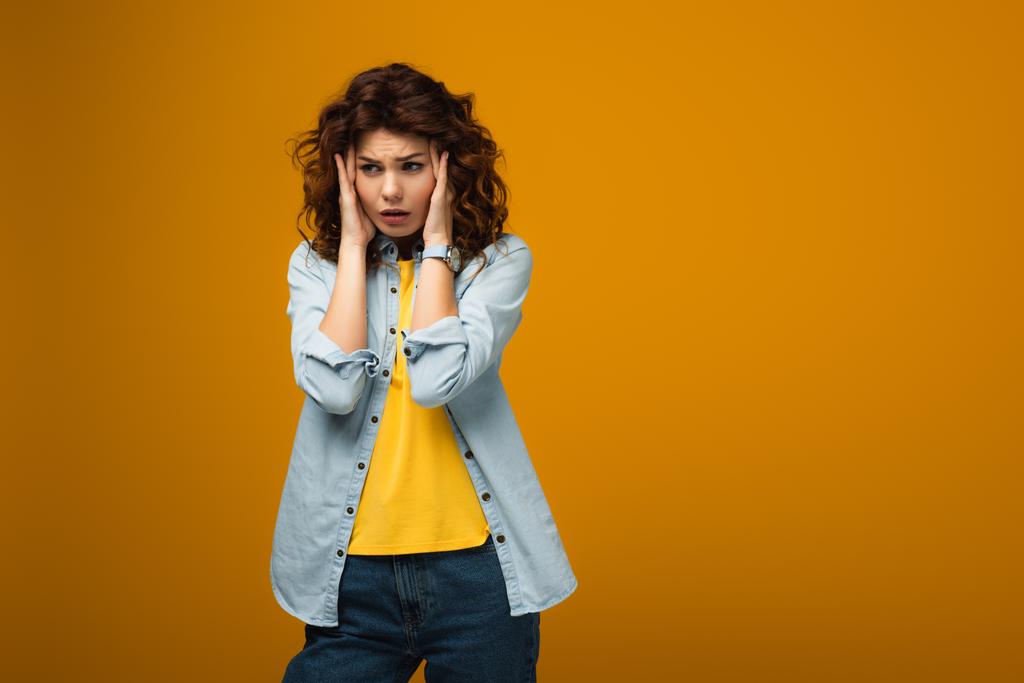 upset curly woman touching head while having migraine on orange  - Photo, Image