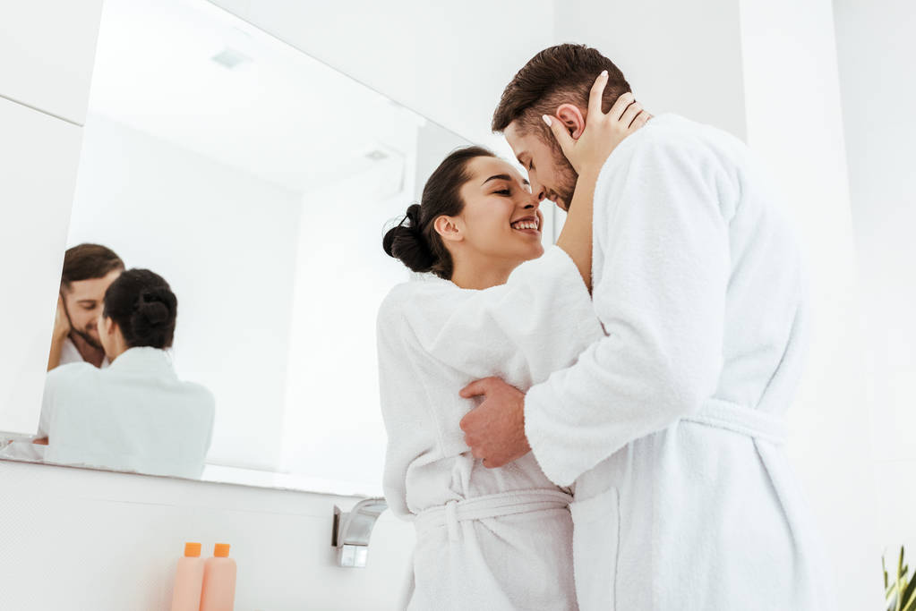 low angle view of happy girl smiling while hugging boyfriend in bathrobe  - Photo, Image