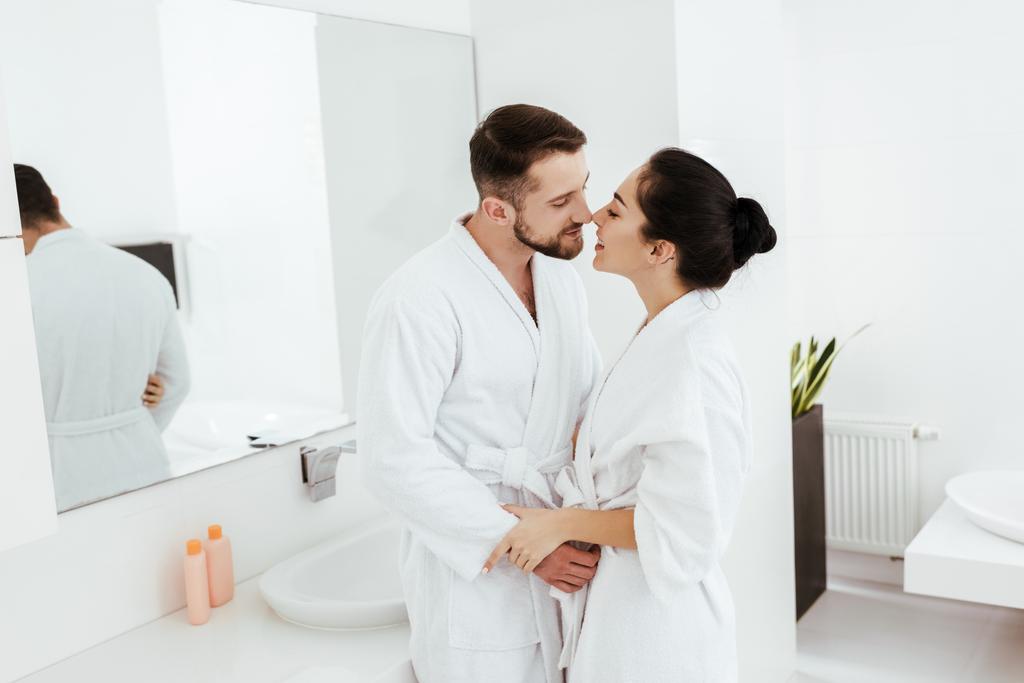 handsome man looking at happy girlfriend standing and smiling in bathrobe  - Photo, Image