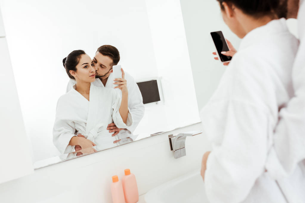 彼氏がバスルームで頬にキスしながら写真を撮る女性の選択的な焦点  - 写真・画像