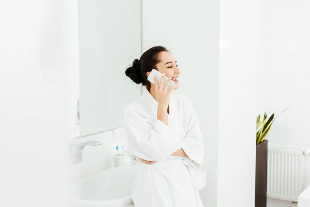 boldog fiatal nőt mosolygós, miközben beszél okostelefon a fürdőszobában  - Fotó, kép