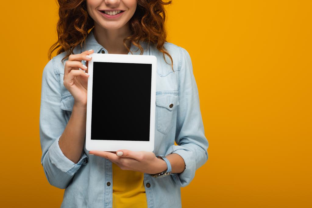 vista cortada de menina encaracolado alegre segurando tablet digital com tela em branco isolado em laranja
  - Foto, Imagem