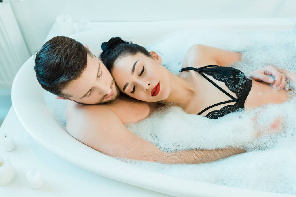 εναέρια όψη του όμορφου άντρα που βρίσκεται στην μπανιέρα με σέξι μελαχρινή γυναίκα σε δαντελωτό σουτιέν  - Φωτογραφία, εικόνα