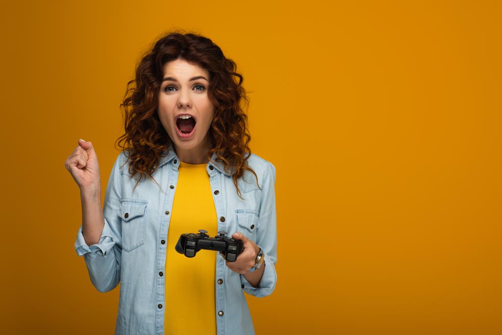 mujer rizada emocional gesto y gritando mientras sostiene el joystick en naranja
  - Foto, imagen