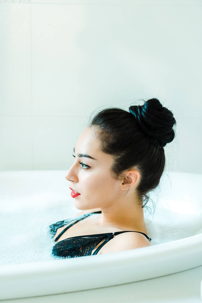Ελκυστική μελαχρινή γυναίκα που βρίσκεται στην μπανιέρα με αφρό μπάνιου  - Φωτογραφία, εικόνα