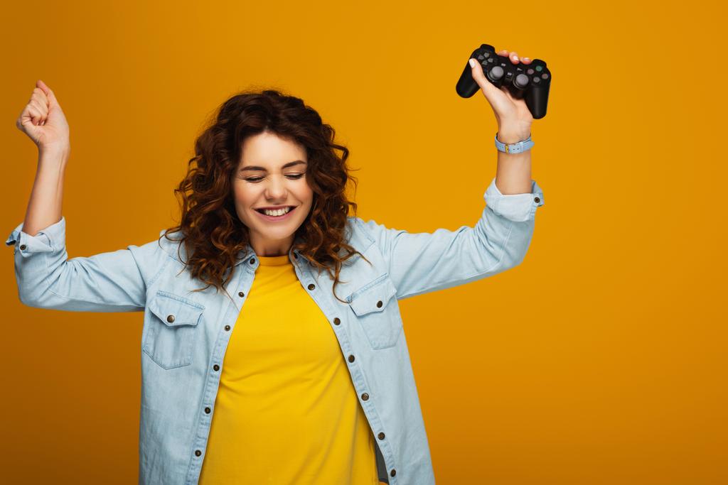 alegre rizado pelirroja chica gesto mientras sostiene joystick en naranja
  - Foto, imagen