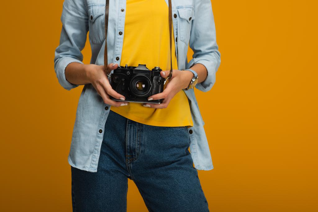 オレンジ色のデジタルカメラを立って持っている若い女性のトリミングされたビュー  - 写真・画像