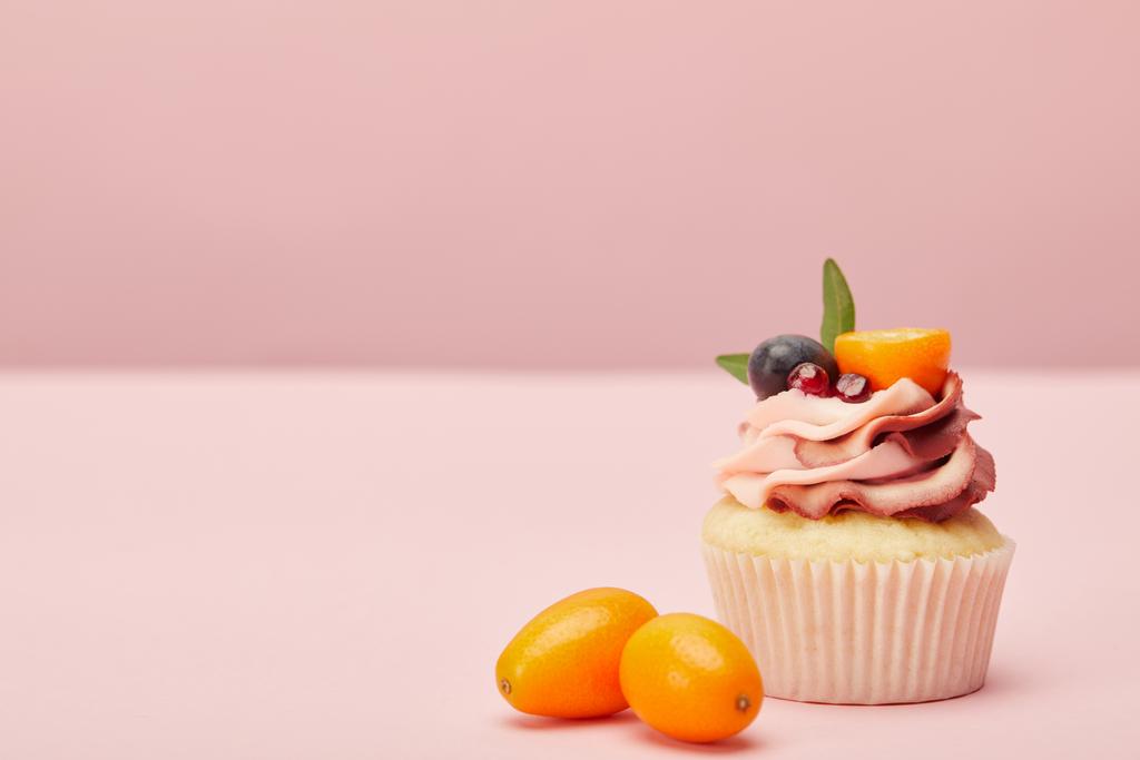 zoete cupcake met room en twee kumquats op roze oppervlak - Foto, afbeelding