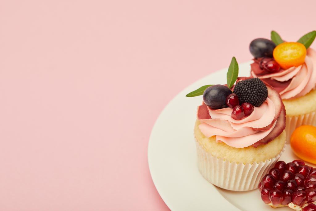süße Cupcakes mit Beeren und Früchten auf Teller auf rosa Oberfläche - Foto, Bild