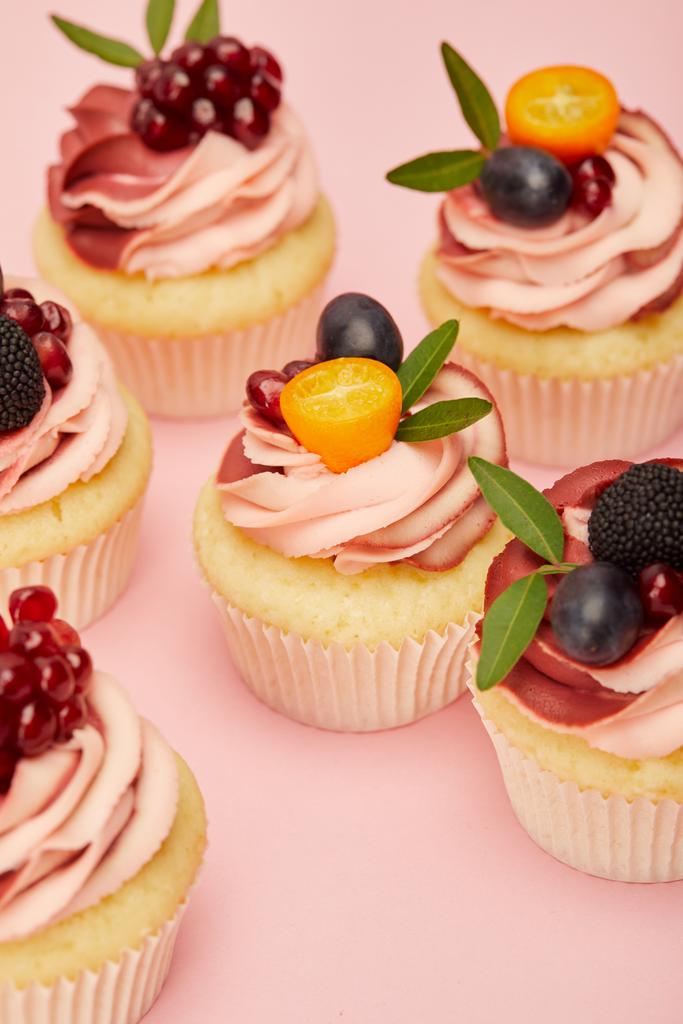zoete Cupcakes met fruit en bessen op roze oppervlak - Foto, afbeelding