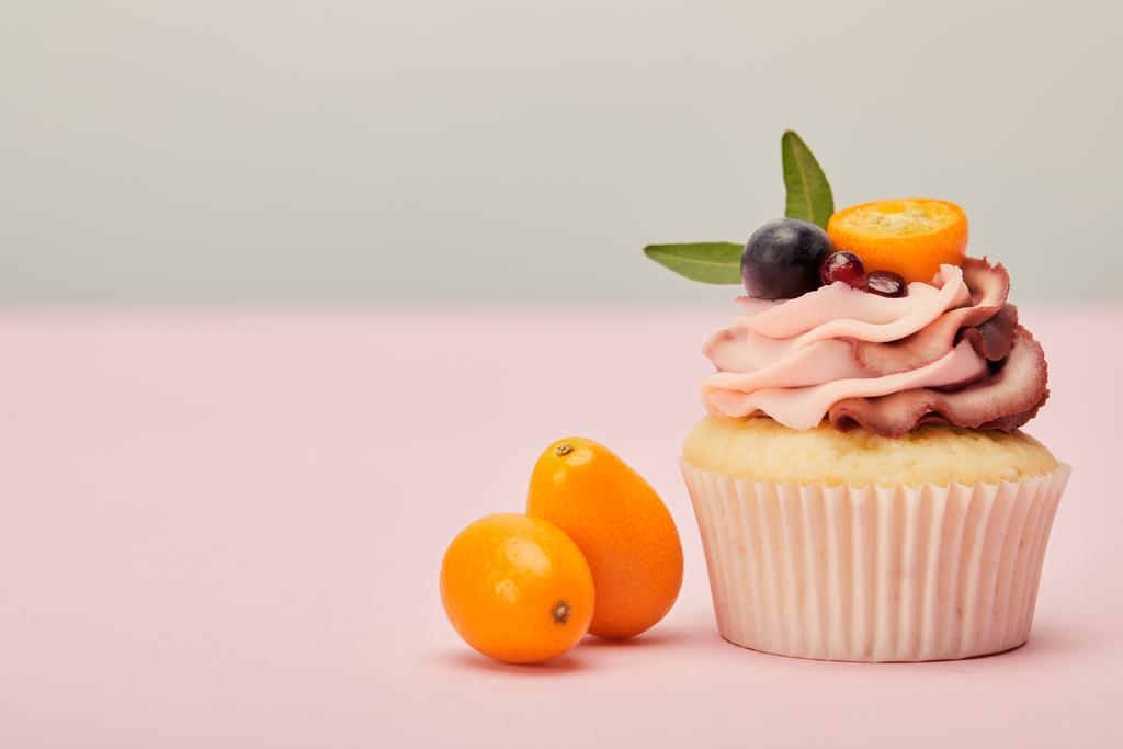 cupcake with ripe kumquats on pink surface isolated on grey - Photo, Image