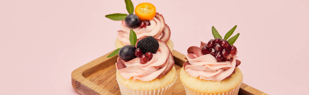 plano panorámico de cupcakes con frutas y bayas en bandeja de madera aislada en rosa
 - Foto, Imagen