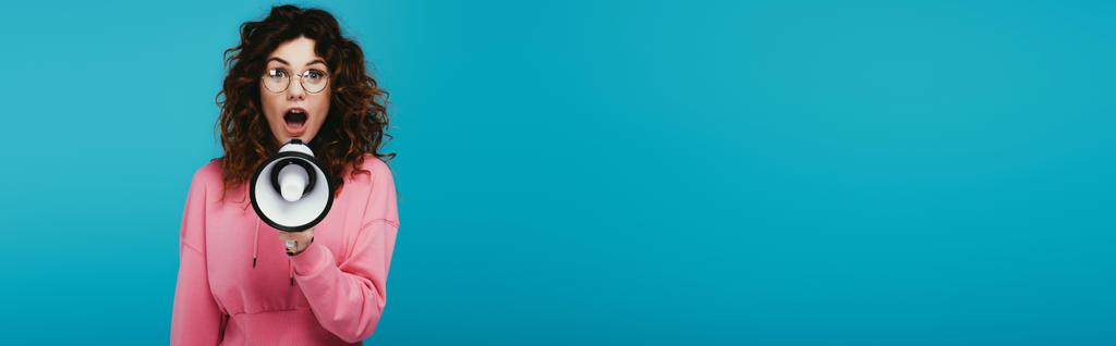 панорамный снимок привлекательной рыжеволосой девушки, кричащей, держа мегафон на синем
  - Фото, изображение