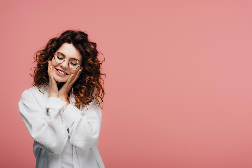 happy curly woman in glasses smiling while touching face on pink - Photo, Image