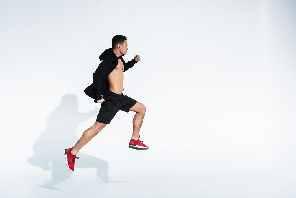 Вид сбоку спортивного мужчины смешанной расы в черной одежде, бегущего на белом
 - Фото, изображение