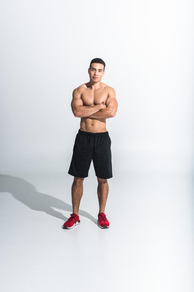 handsome sportive mixed race man in black shorts and red sneakers looking at camera on white - Photo, Image